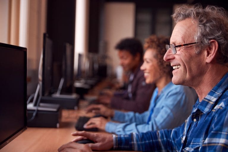 Group Of Mature Adult Students In Class Working At Computers In College Library